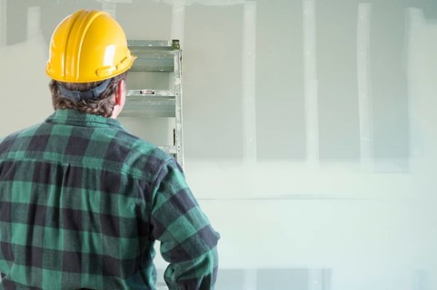 Contractor in hard hat looking at drywall
