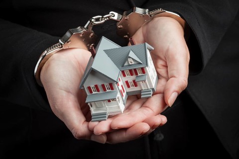 Woman in handcuffs holding small house against black