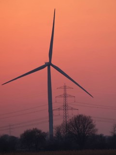 Wind turbine and high-voltage power line against the evening sky in Hamburg's Vier- und Marschlanden