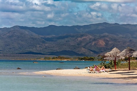 Couple lying on sun lounger on beach with parasol
