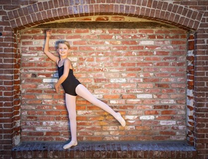 Cute caucasian ballerina girl posting against A brick wall