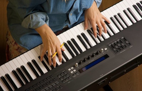 Woman's fingers with pencil on digital piano keys