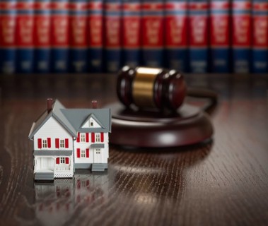 Gavel and small model house on wooden table with law books in background