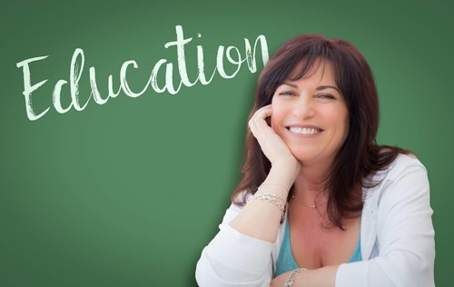 Education written on green chalkboard behind smiling middle aged woman