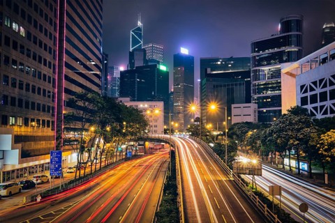 Street traffic in Hong Kong at night. Office skyscraper buildings and busy traffic on highway road with blurred cars light trails. Hong Kong