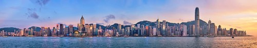 Panorama of Hong Kong skyline cityscape downtown skyscrapers over Victoria Harbour in the evening with junk tourist ferry boat on sunset with dramatic sky. Hong Kong