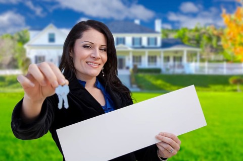 Hispanic woman holding blank sign and keys in front of beautiful house