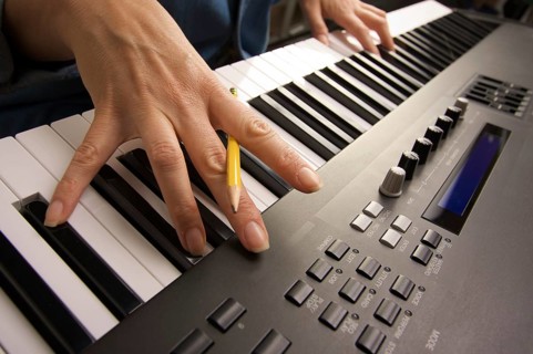 Woman's fingers with pencil on digital piano keys