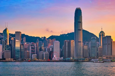 Hong Kong skyline cityscape downtown skyscrapers over Victoria Harbour in the evening with junk tourist ferry boat on sunset with dramatic sky. Hong Kong