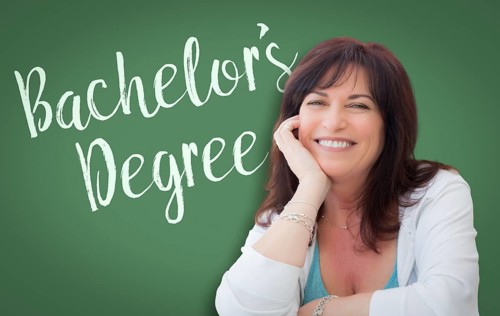Bachelor's degree written on green chalkboard behind smiling middle aged woman
