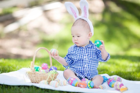 mixed-race chinese and caucasian baby boy outside wearing rabbit ears playing with easter eggs