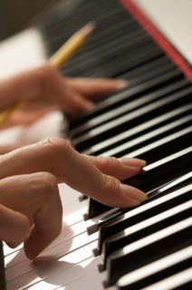 Woman's fingers with pencil on digital piano keys