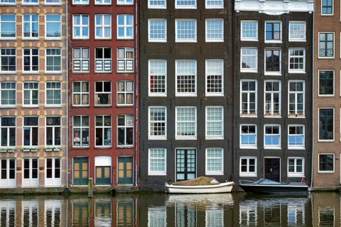 Row of typical houses and boat on Amsterdam canal Damrak with reflection. Amsterdam