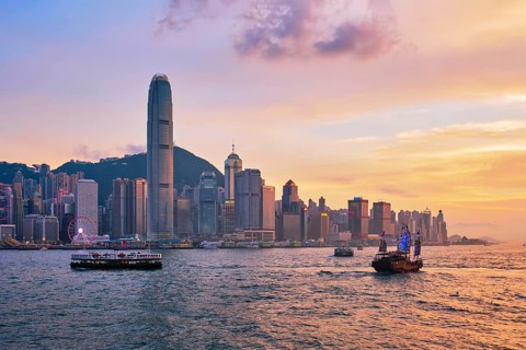 Hong Kong skyline cityscape downtown skyscrapers over Victoria Harbour in the evening with ferry boat and junk boat on sunset. Hong Kong