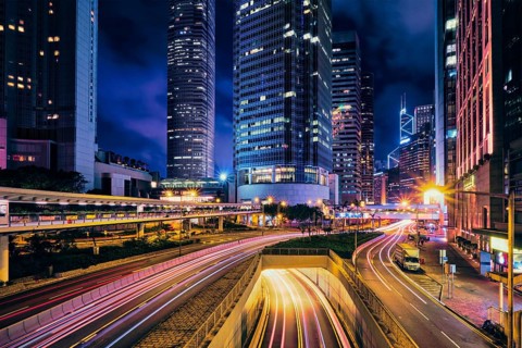 Street traffic in Hong Kong at night. Office skyscraper buildings and busy traffic on highway road with blurred cars light trails. Hong Kong