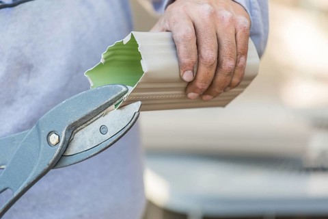 Worker cutting aluminum rain gutter with heavy shears