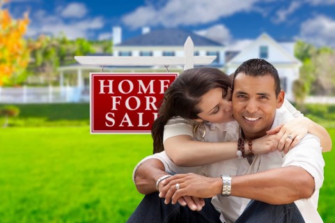 Young happy hispanic young couple in front of their new home and for sale real estate sign
