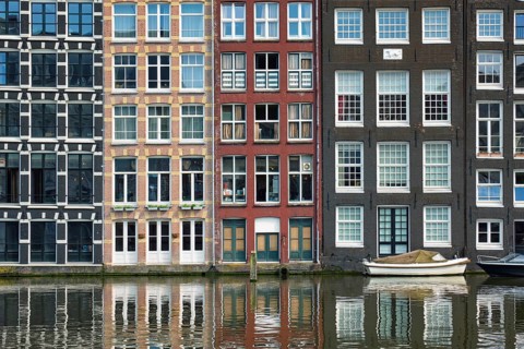 Row of typical houses and boat on Amsterdam canal Damrak with reflection. Amsterdam
