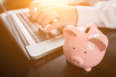 Piggy bank near male hands typing on laptop computer
