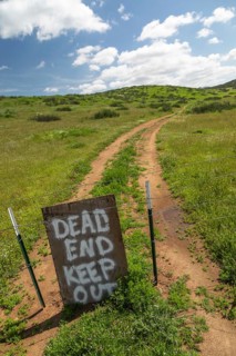 Dead end keep out sign on wire fence at dirt road
