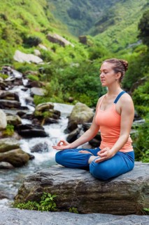 Woman in Hatha yoga asana Padmasana outdoors at tropical waterfall