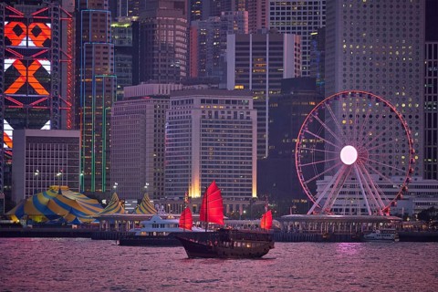 Tourist junk boat ferry with red sails and Hong Kong skyline cityscape downtown skyscrapers over Victoria Harbour in the evening. Hong Kong
