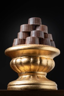 Stack of fine chocolates on golden pillar dish with dark background