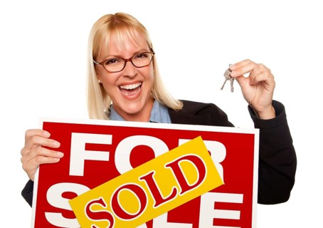 Attractive blonde holding keys & sold for sale sign isolated on a white background