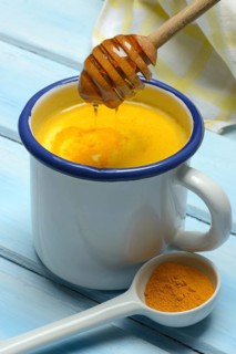 Kurkuma-Milch in Tasse und Honigloeffel mit herablaufendem Bienenhonig und Kurkumapulver