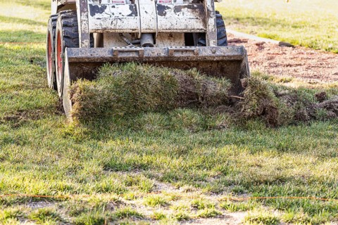 Small bulldozer removing grass from yard preparing for pool installation