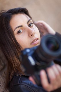 Young adult ethnic female photographer against wall holding camera