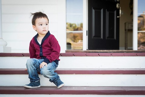 Cute melancholy mixed-race boy sitting on front porch steps