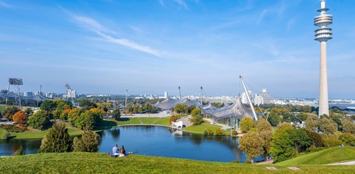 Two people sitting in the park with Olympic lake and Olympic tower