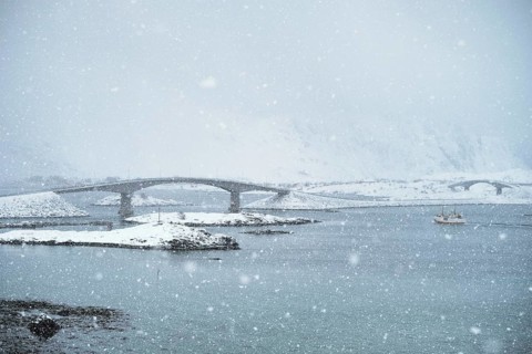 Fredvang bridges in heavy snowfall in winter with fishing ship. Lofoten islands