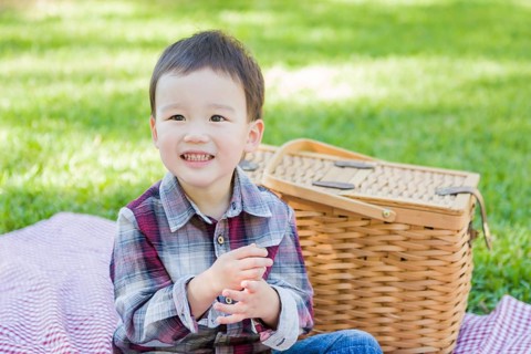 Cute young mixed-race boy sitting in park near picnic basket