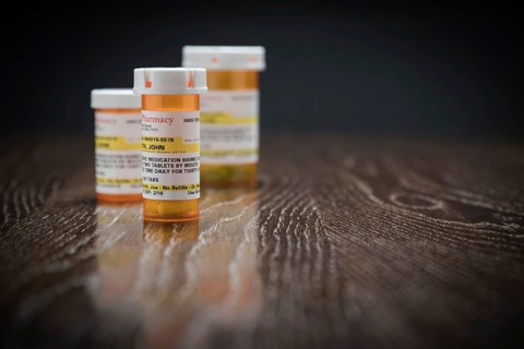 Variety of non-proprietary prescription medicine bottles on reflective wooden surface