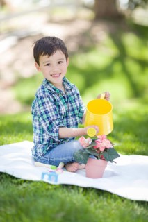 mixed-race young boy watering his potted flowers outside on the grass