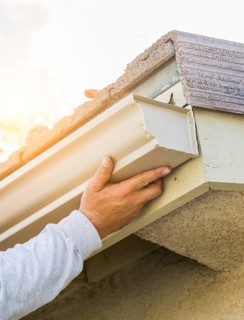 Worker attaching aluminum rain gutter to fascia of house
