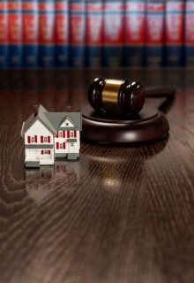 Gavel and small model house on wooden table with law books in background