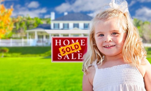 Cute smiling girl in front yard with sold for sale real estate sign and house