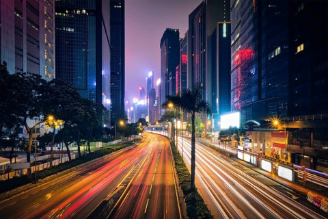 Street traffic in Hong Kong at night. Office skyscraper buildings and busy traffic on highway road with blurred cars light trails. Hong Kong