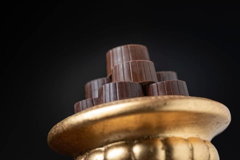 Stack of fine chocolates on golden pillar dish with dark background