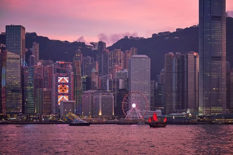 Tourist junk boat ferry with red sails and Hong Kong skyline cityscape downtown skyscrapers over Victoria Harbour in the evening. Hong Kong