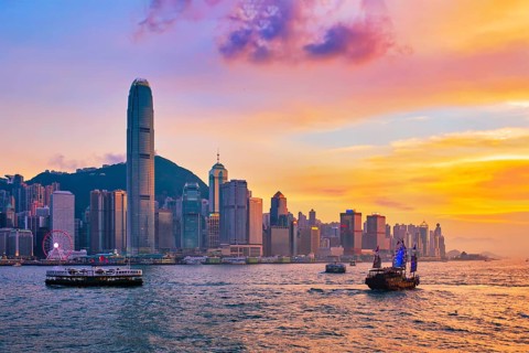 Hong Kong skyline cityscape downtown skyscrapers over Victoria Harbour in the evening with ferry boat and junk boat on sunset. Hong Kong