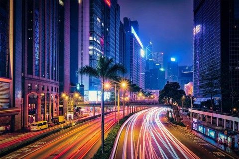 Street traffic in Hong Kong at night. Office skyscraper buildings and busy traffic on highway road with blurred cars light trails. Hong Kong