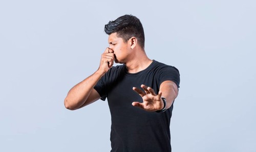 Confused unhappy man grabbing nose with fingers and stretching hand out feeling disgusted