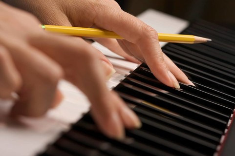 Woman's fingers with pencil on digital piano keys