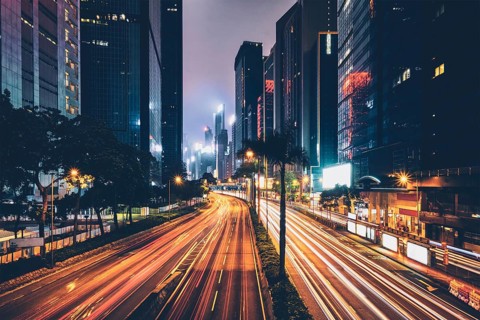 Street traffic in Hong Kong at night. Office skyscraper buildings and busy traffic on highway road with blurred cars light trails. Hong Kong