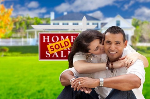 Young happy hispanic young couple in front of their new home and sold for sale real estate sign