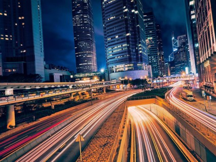 Street traffic in Hong Kong at night. Office skyscraper buildings and busy traffic on highway road with blurred cars light trails. Hong Kong